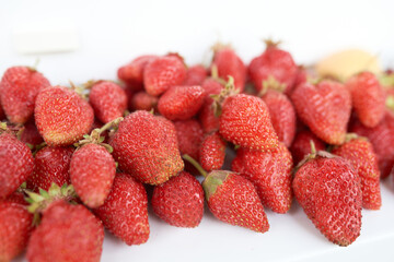 A lot of strawberries and one yellow apricot with green leaf lie on a white windowsill