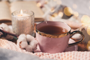 Details of still life in the home interior of living room. Sweater, cup of tea, cotton, cozy, book, candle. Moody. Cosy autumn winter concept. Decoration, vintage with glow bokeh.