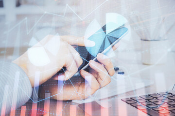 Double exposure of man's hands holding and using a digital device and forex graph drawing. Financial market concept.