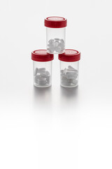 Transparent pill bottles with some pills inside and red caps forming a pyramid on white background