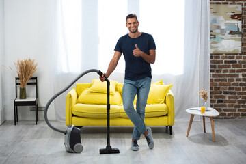 Fototapeta na wymiar man showing thumb up while standing near vacuum cleaner in living room