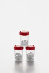 Transparent pill bottles with some pills inside and red caps forming a pyramid on white background