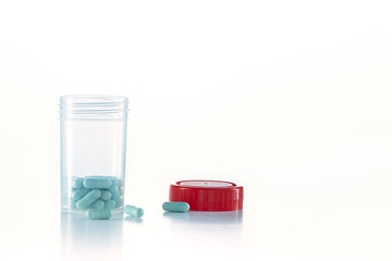 open transparent pill bottle with some pills outside and red caps on the white ground