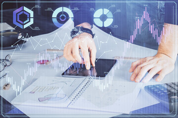 Double exposure of man's hands holding and using a digital device and forex graph drawing. Financial market concept.