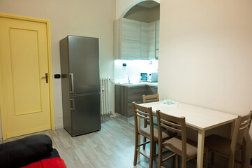 View of the interior of a small living room with kitchen of a two-room apartment. The kitchen led under-cabinet light attracts attention. Gray laminate wood flooring, matching the walls and kitchen.