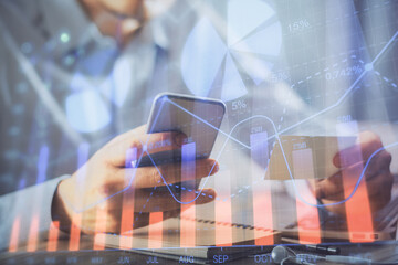 Double exposure of man's hands holding and using a phone and financial graph drawing. Analysis concept.