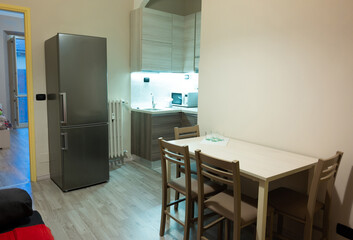View of the interior of a small living room with kitchen of a two-room apartment. The kitchen led under-cabinet light attracts attention. Gray laminate wood flooring, matching the walls and kitchen.