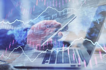 Double exposure of man's hands holding and using a phone and financial graph drawing. Analysis concept.