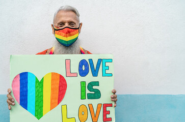 Senior gay man wearing face protective mask celebrating gay pride festival during corona virus...