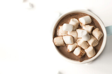 A mug of chocolate drink with marshmallows on a light background with bokeh.