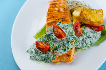 Grilled salmon steak. A piece of red fish on a white plate and a blue background on the table. Fish food with sauce, tomatoes, lemon. Restaurant menu. Grill fried.