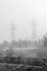 Two pylons in the fog on the outskirts of the city. Black and white with grain. Vertical view.