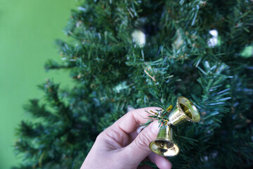 Close up of hand holding the small gold bell hangs on the Christmas tree. Concept during the Merry...