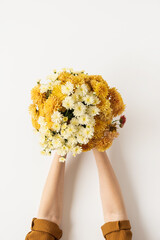 Flatlay of yellow and ginger fall wild flowers bouquet in women's hands isolated on white...