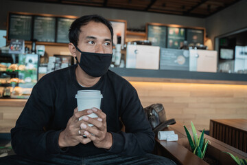 Man waiting in a cafe while enjoying coffee with face mask for healthy