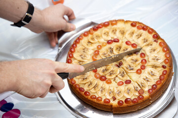 Man cuts homemade pie lying on round Board into pieces with knife.
