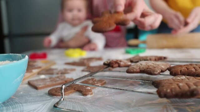 The mother holds the baby in her arms and shows him a gingerbread. Gingerbread in the foreground. In the background, a woman rolls out the dough with a rolling pin. The concept of family cooking
