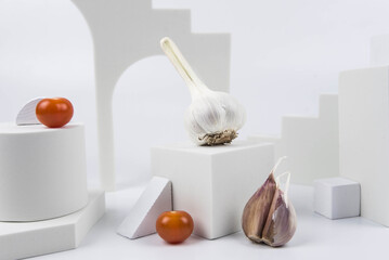 Aesthetic food photography on trendy white podium. Minimal food art still life concept.  Garlic and cherry tomatoes on white background.