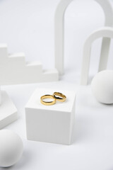 Golden wedding rings on trendy white podium. Aesthetic still life art photography.