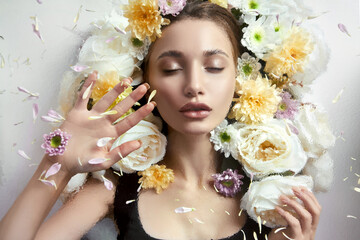 Naklejka premium Beauty portrait of a woman with flowers and petals behind the glass in drops of rain. Cosmetics for the face, moisturizing the skin. Out of focus, selective focus and noise