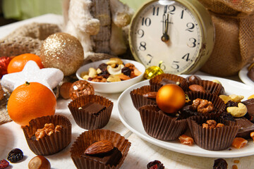 sweet food background for christmas or holiday decoration - chocolate candies, tangerines, nuts and dried fruits on white wood