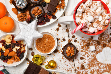 sweet food top view background for merry christmas or new year holiday decoration - chocolate candies, tangerines, cookies, marshmallow and cocoa latte on white wood