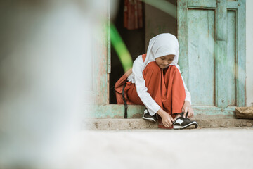 indonesian primary school student getting ready to school in the morning tying shoes in front of the house