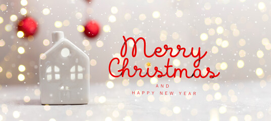 Creative Christmas small toy model house and red balls on white table with light blurred wall background. 2024 Holiday template horizontal composition with Merry Christmas text