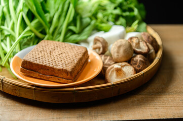 Traditional black herb tofu and vegetables on wooden basket plate. Culinary vegan and vegetarian eating.