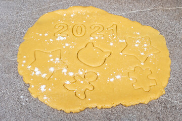 Preparing to make homemade cookies. On yellow dough sprinkled with flour on top, the numbers 2021 and various figures on a gray background, Top view. Christmas decoration food background