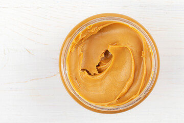 Jar of peanut butter on white wooden table. Space for text.