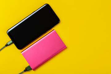 Smartphone Charging with Power Bank on Yelloy Background. Space for text.