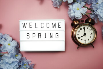 Welcome Spring text in light box and alarm clock with space copy on pink background