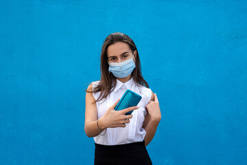 portrait of healthy young business lady wearing medical mask with cell phone on blue background