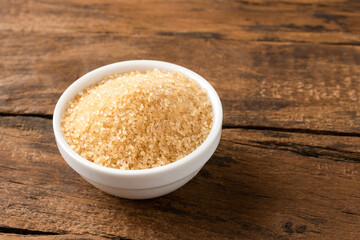 Brown cane sugar in bowl on vintage wooden background