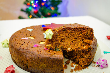 Closeup of a cut Plum Cake for Christmas celebrations. Cake is decorated and a Christmas Tree in the background.