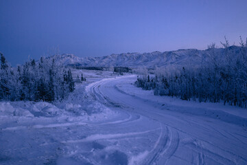 Fototapeta na wymiar Snow covered twilight landscape with a road in Alaska winter