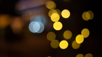 Fototapeta premium Abstract evening night shimmering bokeh background effect street outside near cafe restaurant. Defocused urban city life blur golden light bulbs garlands. Christmas New Year party holiday concept. 
