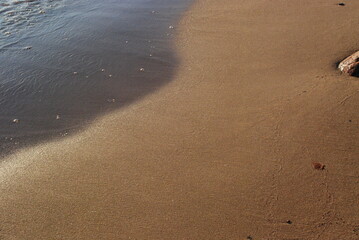 Water and wet sand under the rays of the evening sun.
Autumn evening, sandy coast of the Gulf of Finland. The wave runs over the coastal sand. Two shades of sand due to the water soaked in it. Smooth 