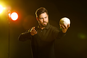 Male actor with human skull on stage - obrazy, fototapety, plakaty