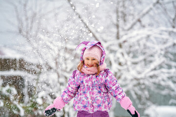 Adorable little girl throws up snow and catches it, in a beautiful winter Park.