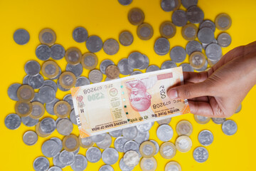 New indian two hundred rupees note in hand and indian coins over yellow background