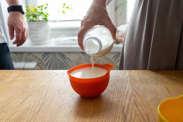 a woman's hand pours milk into a measuring bowl