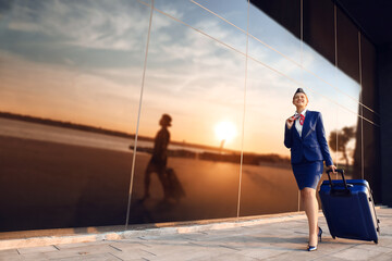 Young stewardess with luggage outdoors