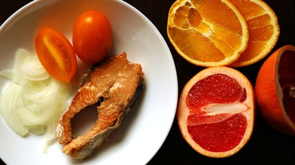 platter for one person of orange food, fish steak, tomato and citrus, top view of a serving of nutritious healthy lunch or dinner of seafood, vegetables and fruits