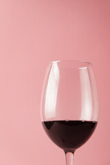 transparent glass goblet of red wine on a pink background.