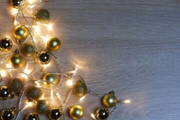 New year christmas composition from golden shiny and matte balls and christmas lights on light wood background with copy space