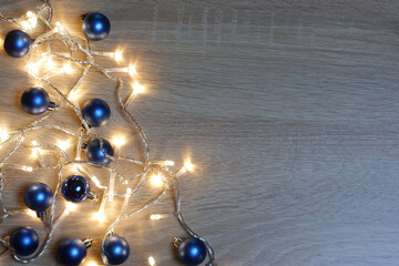 Christmas and New Year composition from blue shiny and matte balls and christmas lights on light wood background with copy space