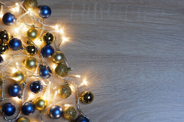 Christmas and New Year composition from blue and gold shiny and matte balls and christmas lights on light wood background with copy space