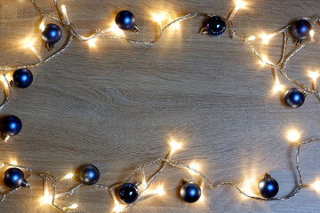 New year christmas frame from blue shiny and matte balls, christmas lights garland on light wood background with copy space